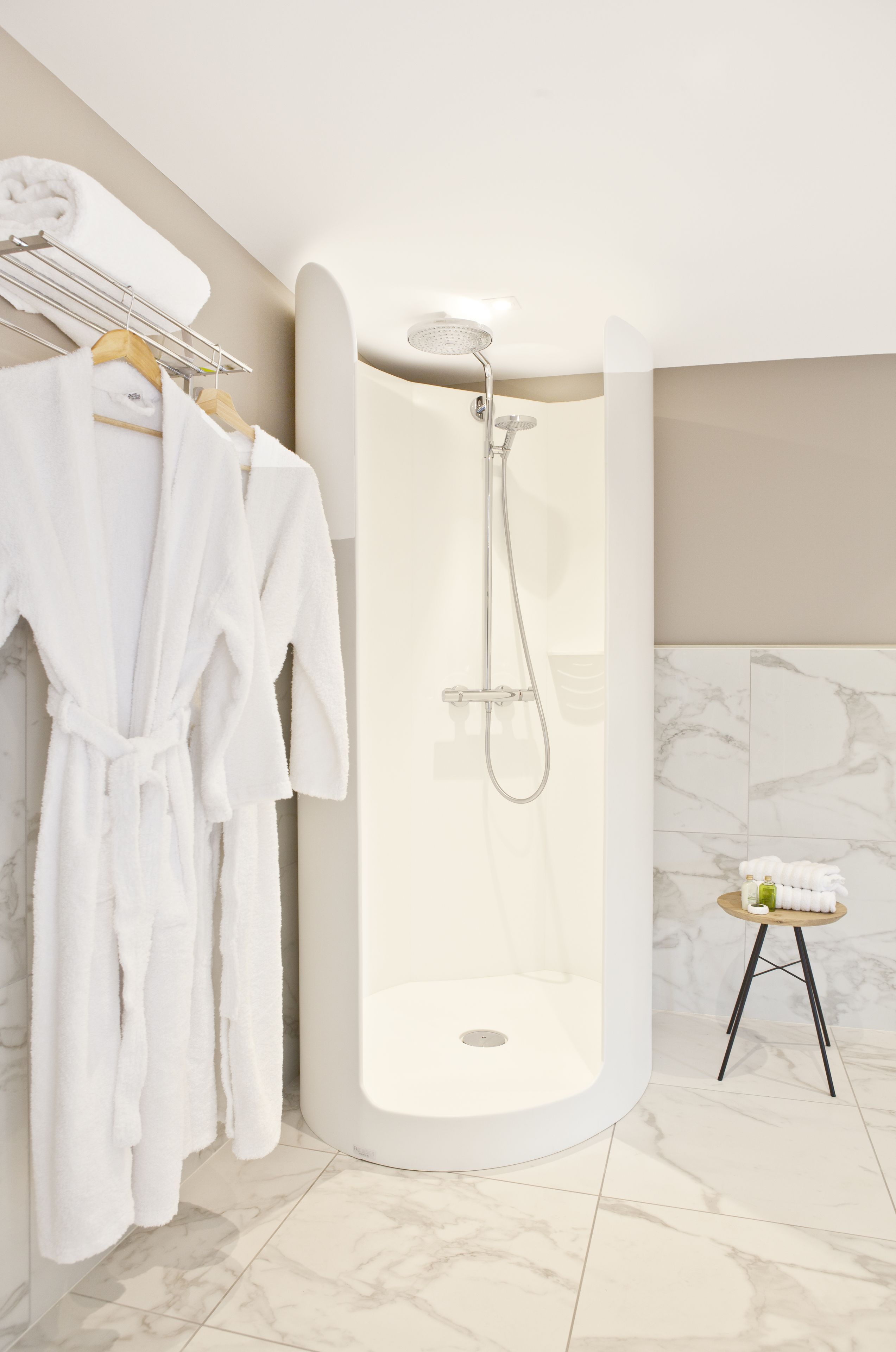 A modern bathroom with a walk-in shower, a robe rack with towels, and a small stool with toiletries.