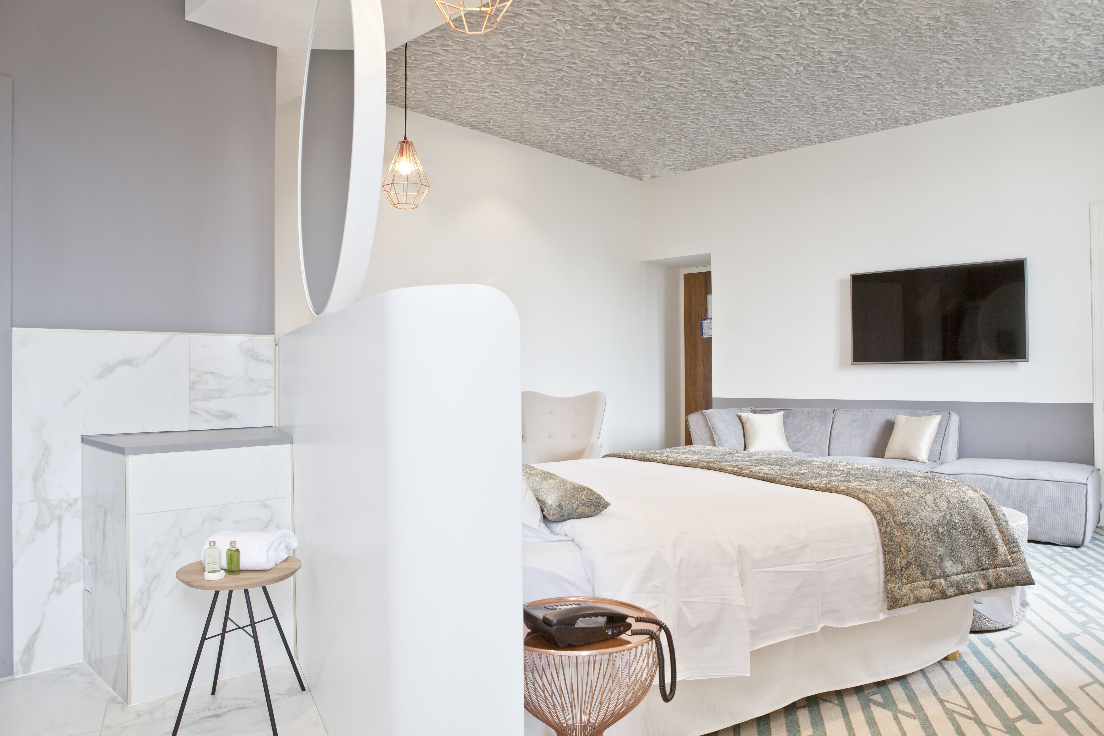 A modern bedroom with a large bed, a TV mounted on the wall, and a small table with toiletries.