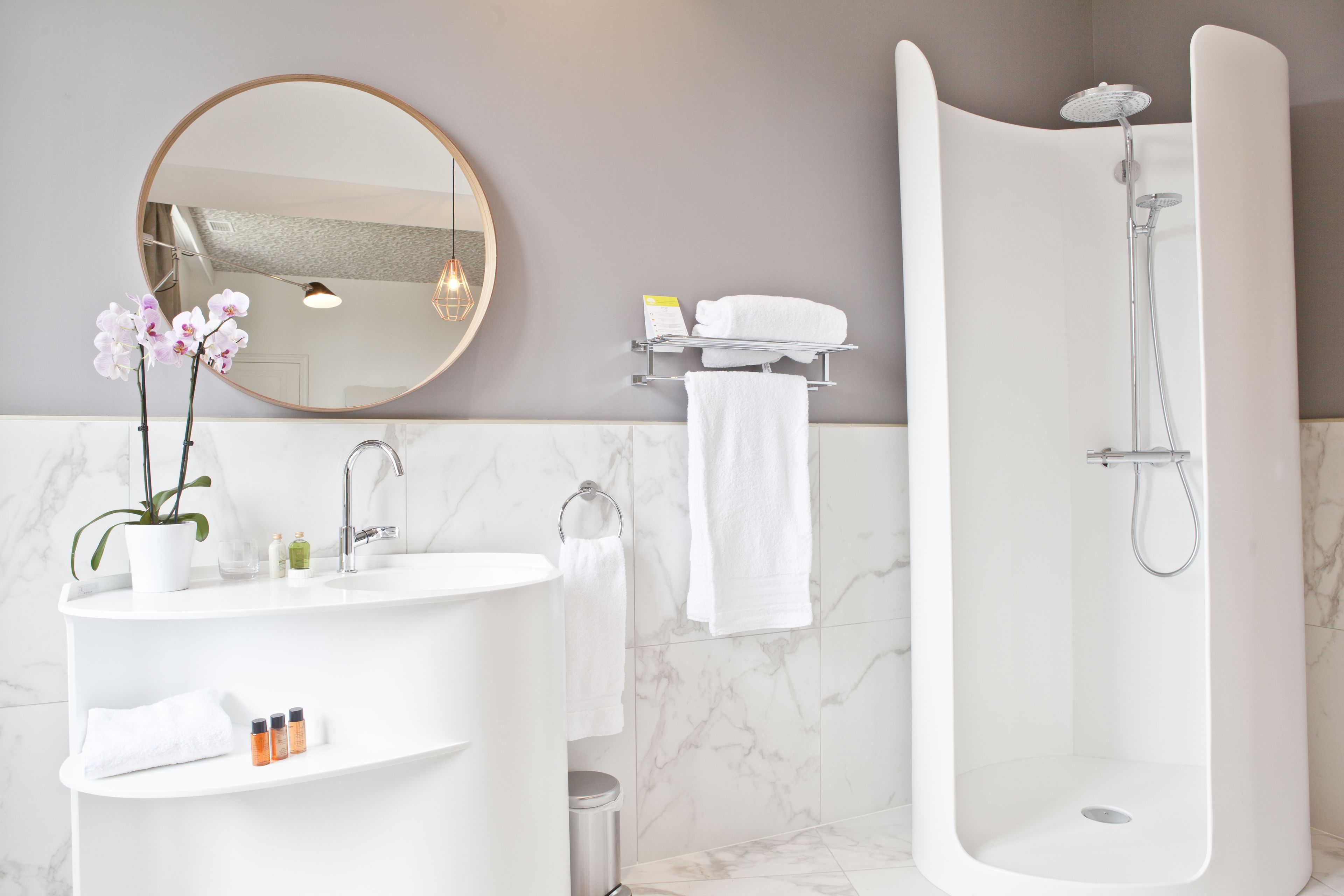 A modern bathroom with a freestanding bathtub, a round mirror, and a white sink with a marble countertop.