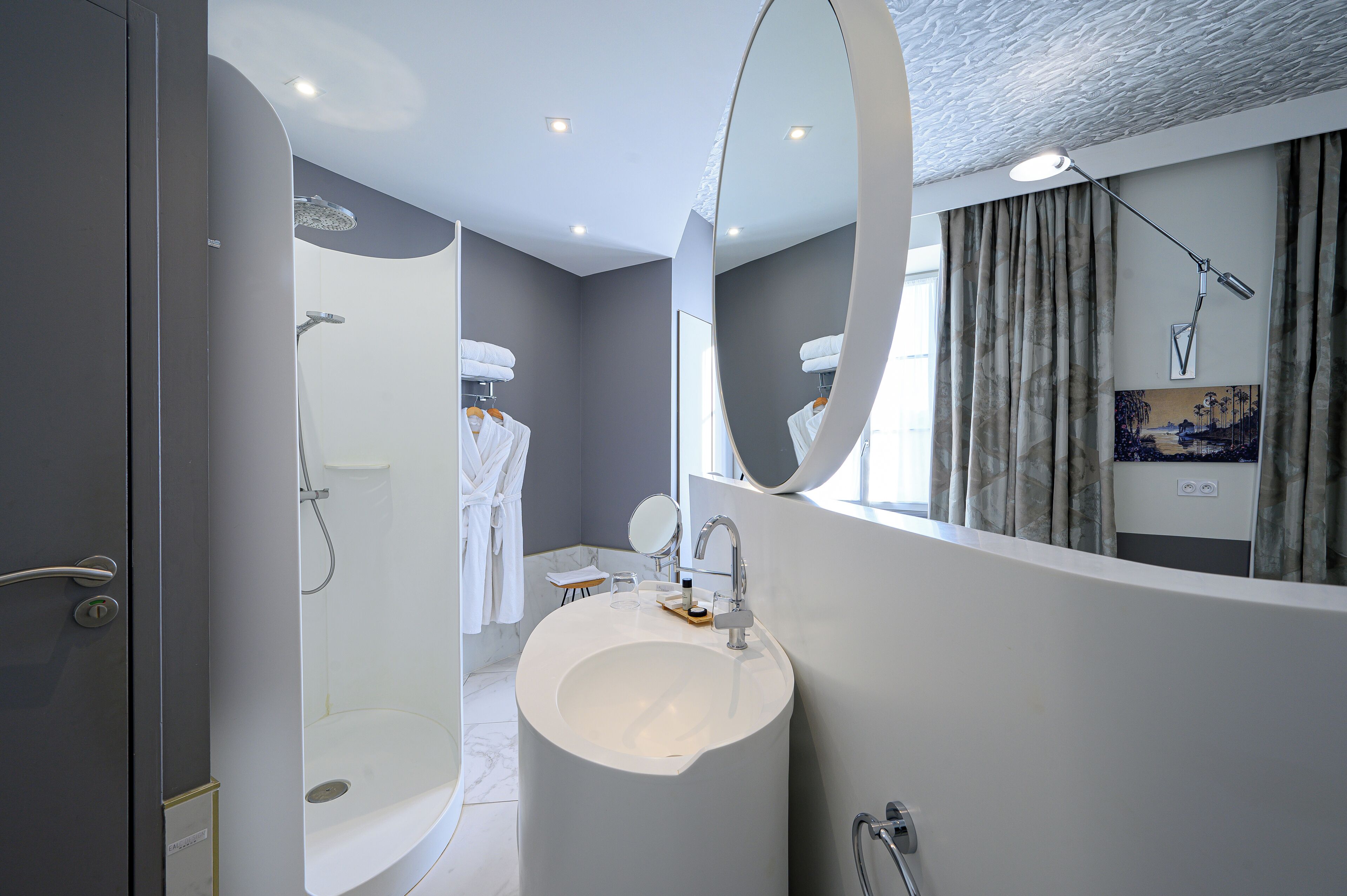 Een moderne badkamer met een groot ovaal wastafel, een ronde spiegel en een douche.