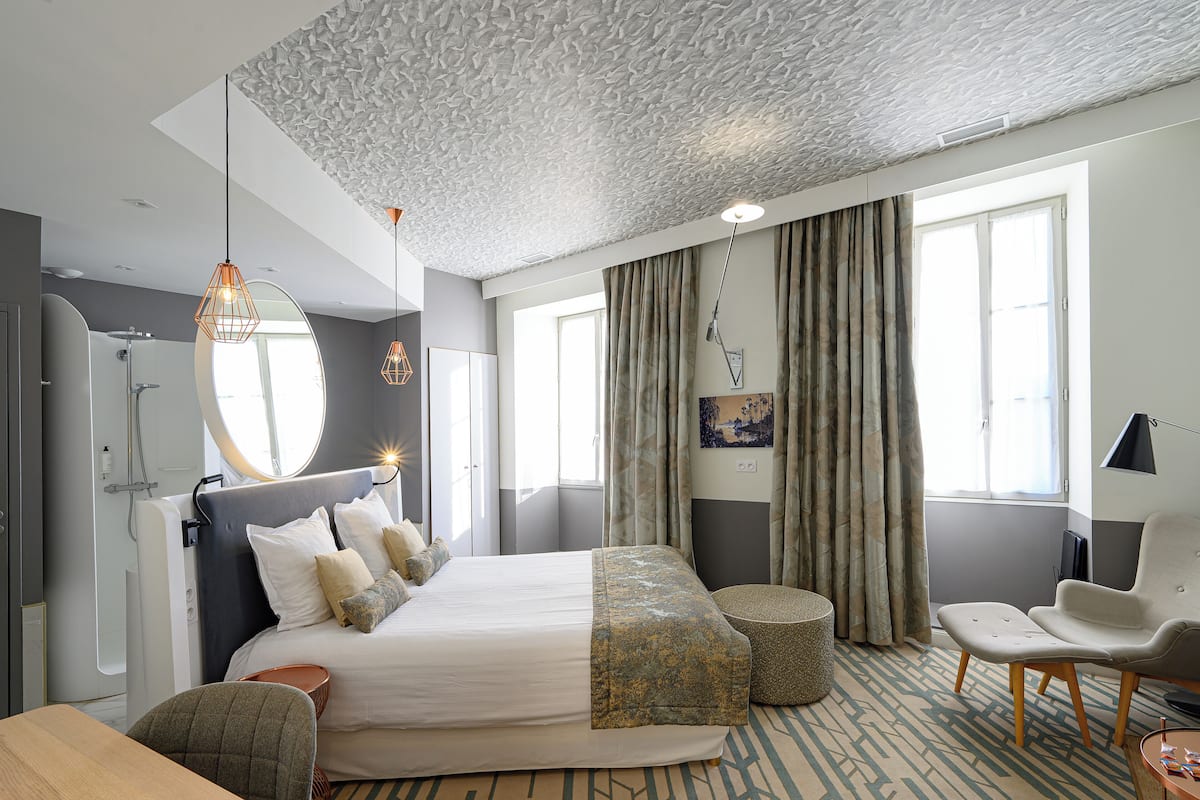 A modern hotel room with a large bed, a sitting area, and a bathroom.