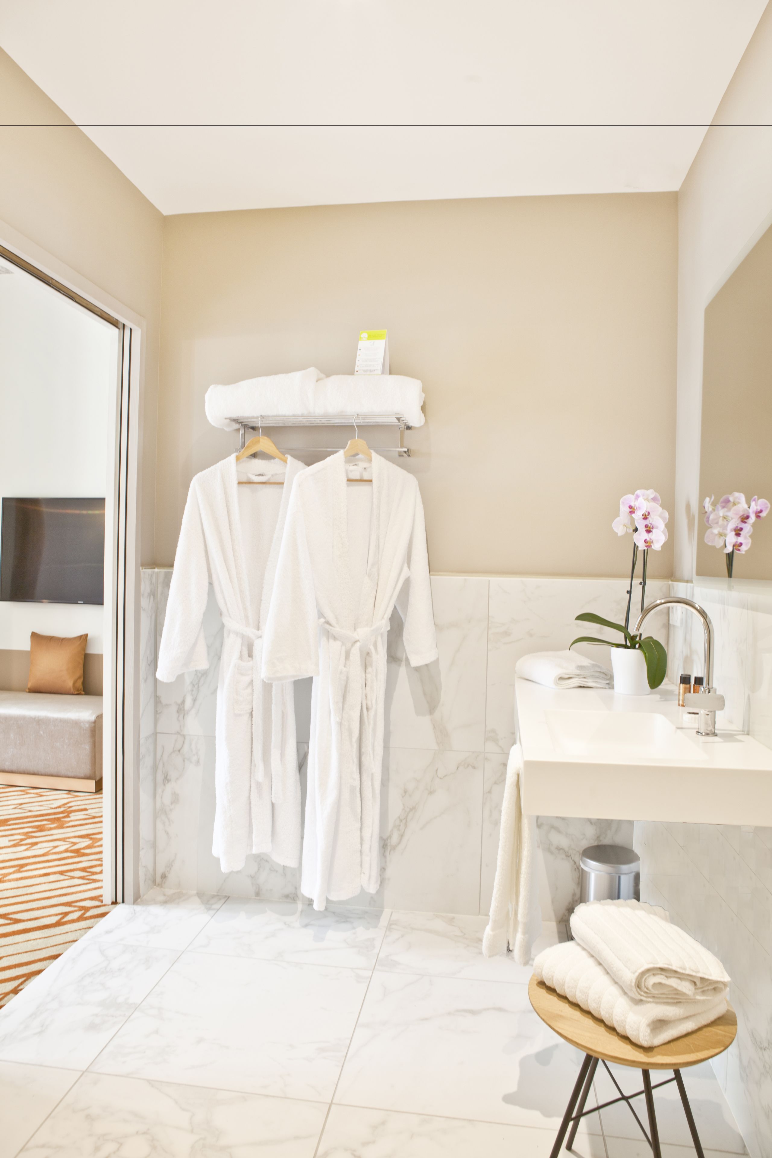 A modern bathroom with marble flooring, a vanity with a sink, and two white robes hanging on a rack.