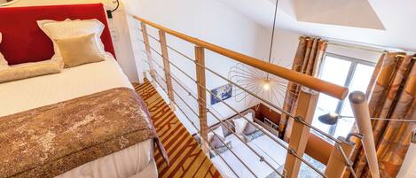 A high-ceilinged room with a bed, a red headboard, and a patterned carpet.