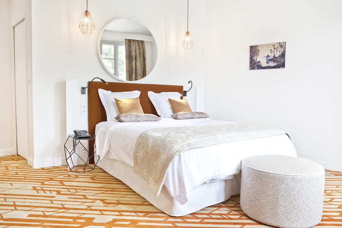 A neatly arranged bedroom with a bed, bedside table, and a round ottoman.