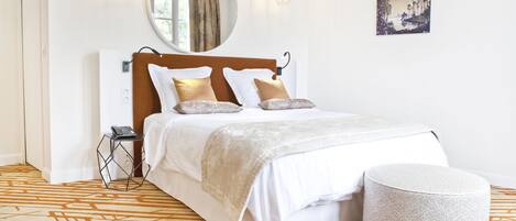 A neatly arranged bedroom with a bed, bedside table, and a round ottoman.