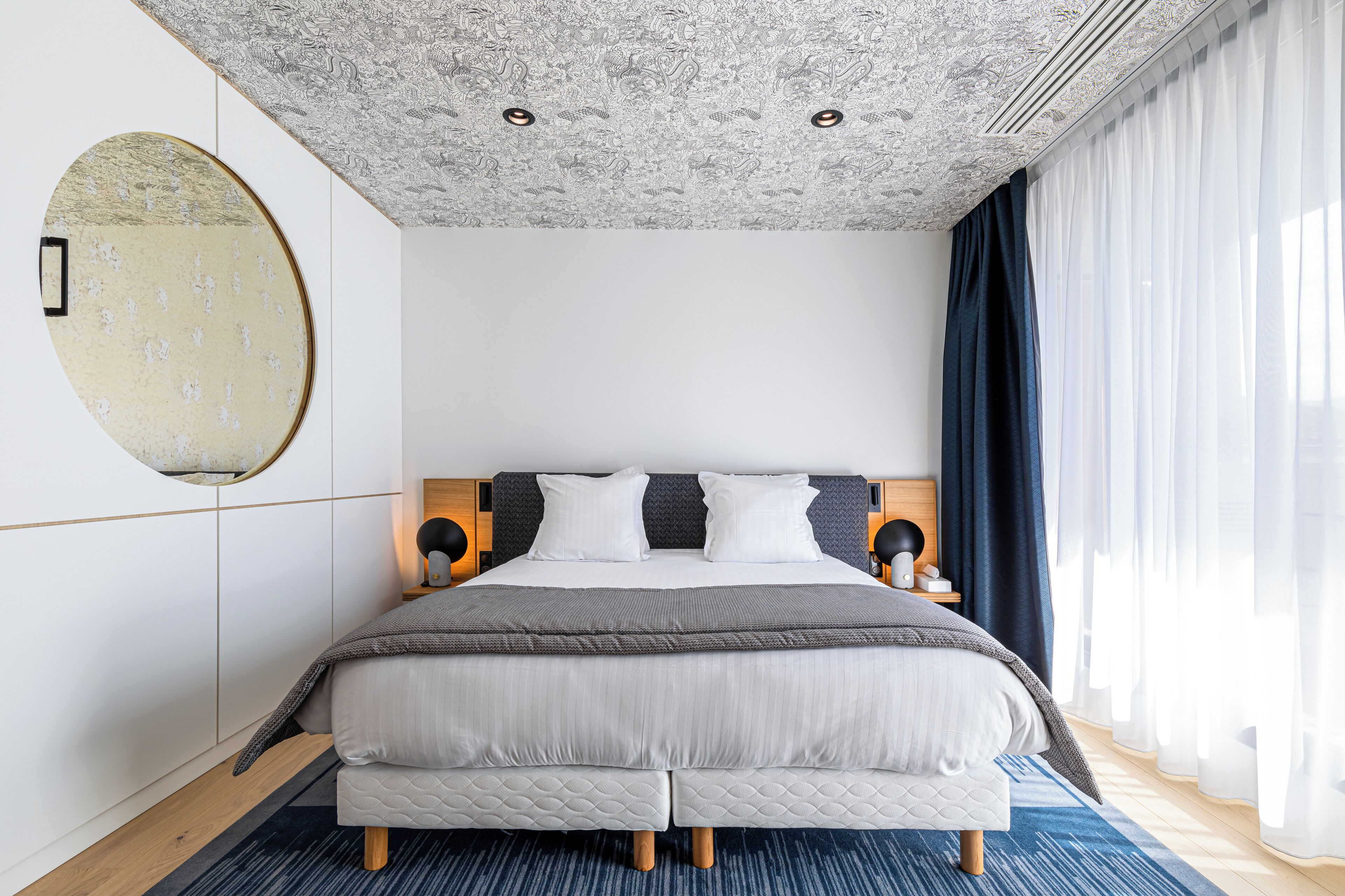 Un dormitorio moderno con una cama grande, un espejo redondo y un techo con diseños intrincados.