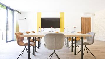 Ein Konferenzraum mit einem langen Tisch, mehreren Stühlen, einem Flachbildfernseher und einer Tür mit Holzverkleidung.