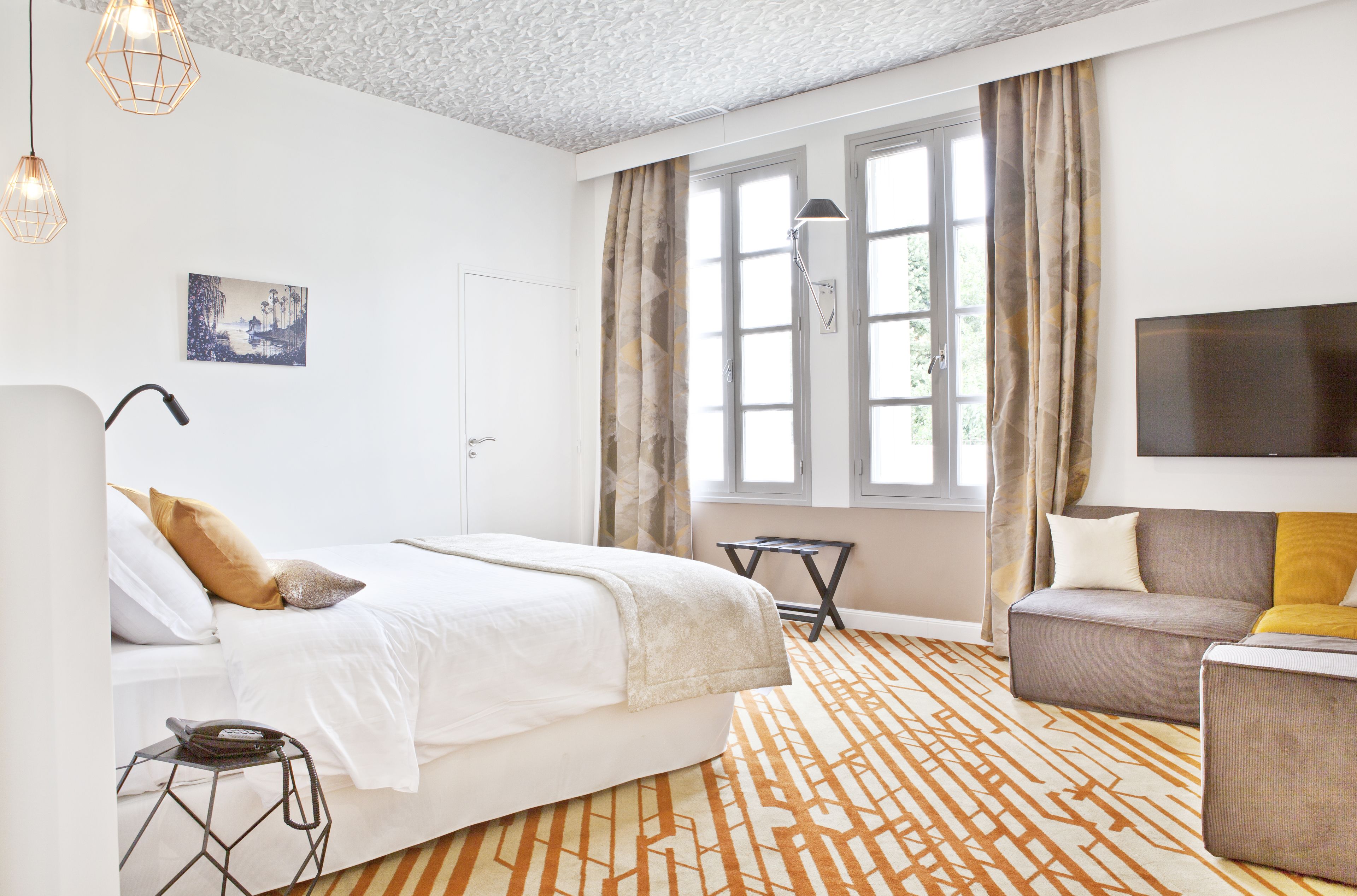 A modern hotel room with a large bed, a sofa, a TV, and a window with curtains.