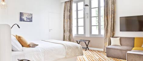 A modern hotel room with a large bed, a sofa, a TV, and a window with curtains.