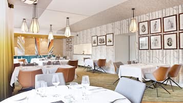 En restaurant med flere spiseborde, stole og hængende lamper.