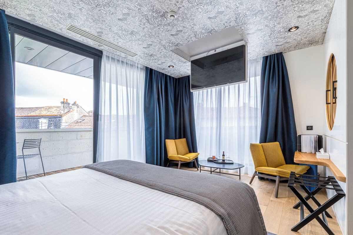 A hotel room with a large bed, two chairs, a small table, and a TV.