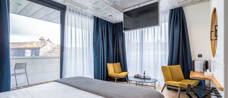 A hotel room with a large bed, two chairs, a small table, and a TV.