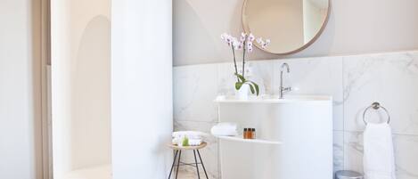 A modern bathroom with a curved shower, a sink with a mirror, and a small stool with toiletries.