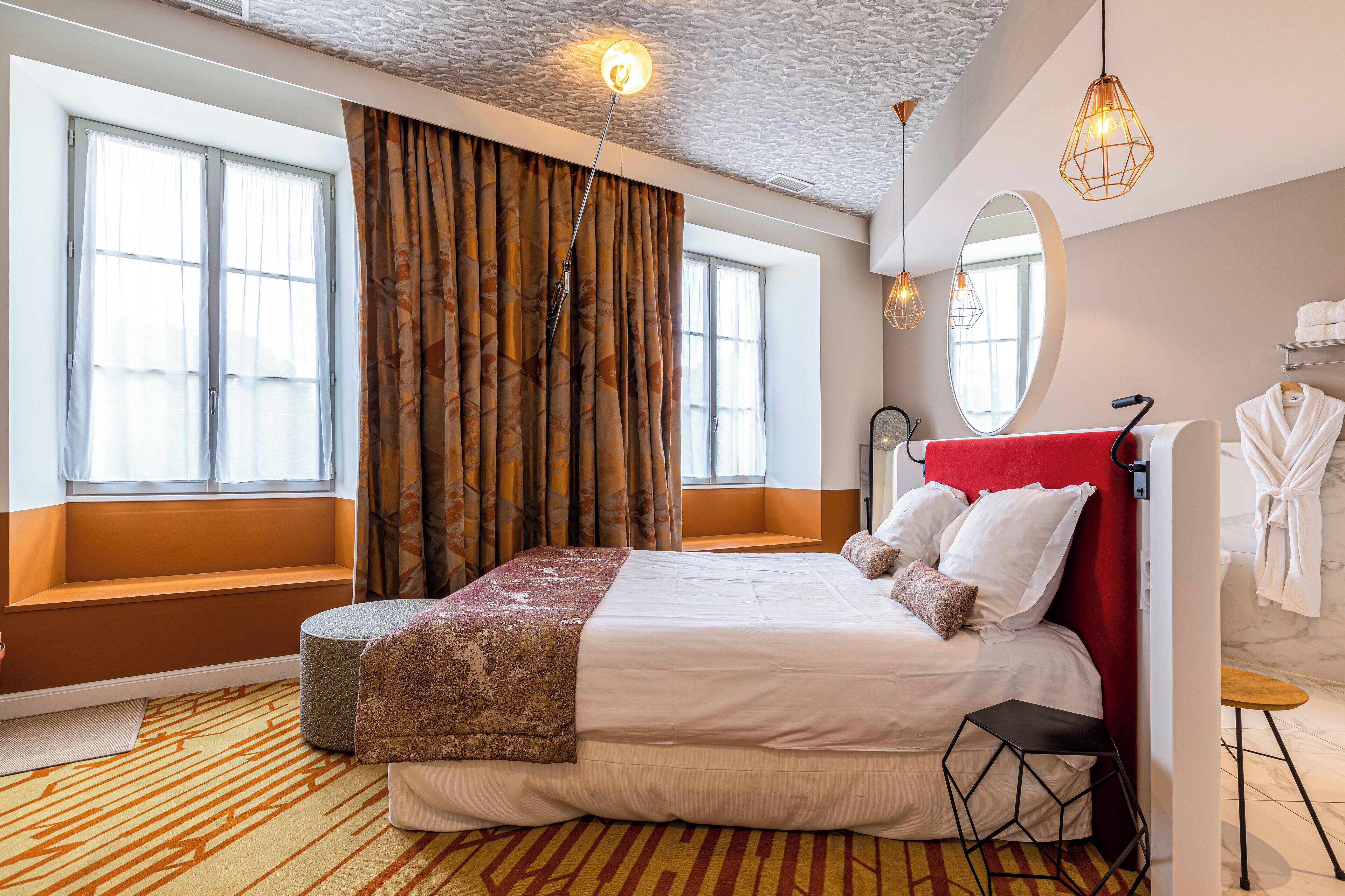 Une chambre d’hôtel avec un grand lit, un coin salon, un miroir et une fenêtre avec des rideaux.