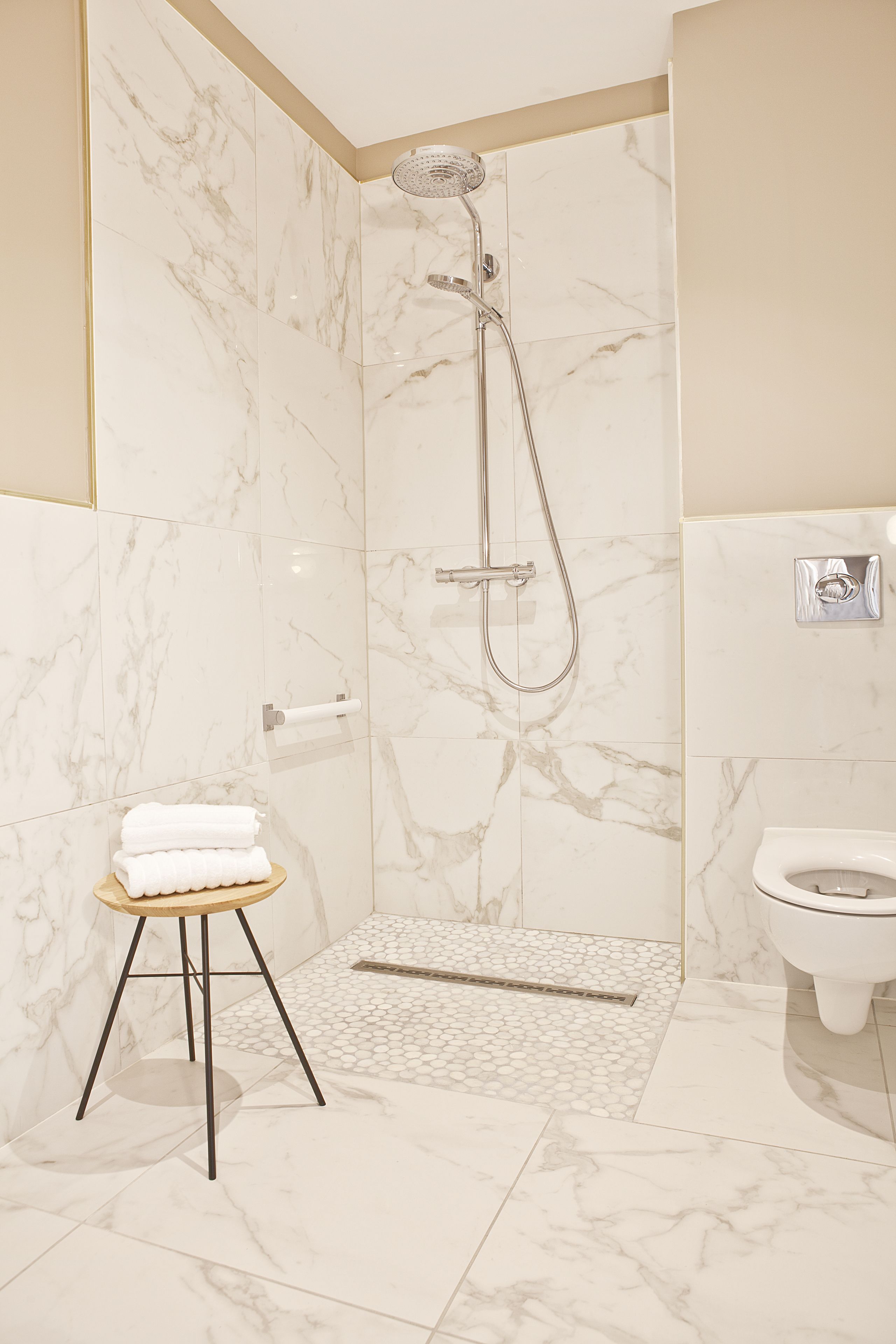 Un baño moderno con ducha, inodoro y un taburete pequeño con toallas.