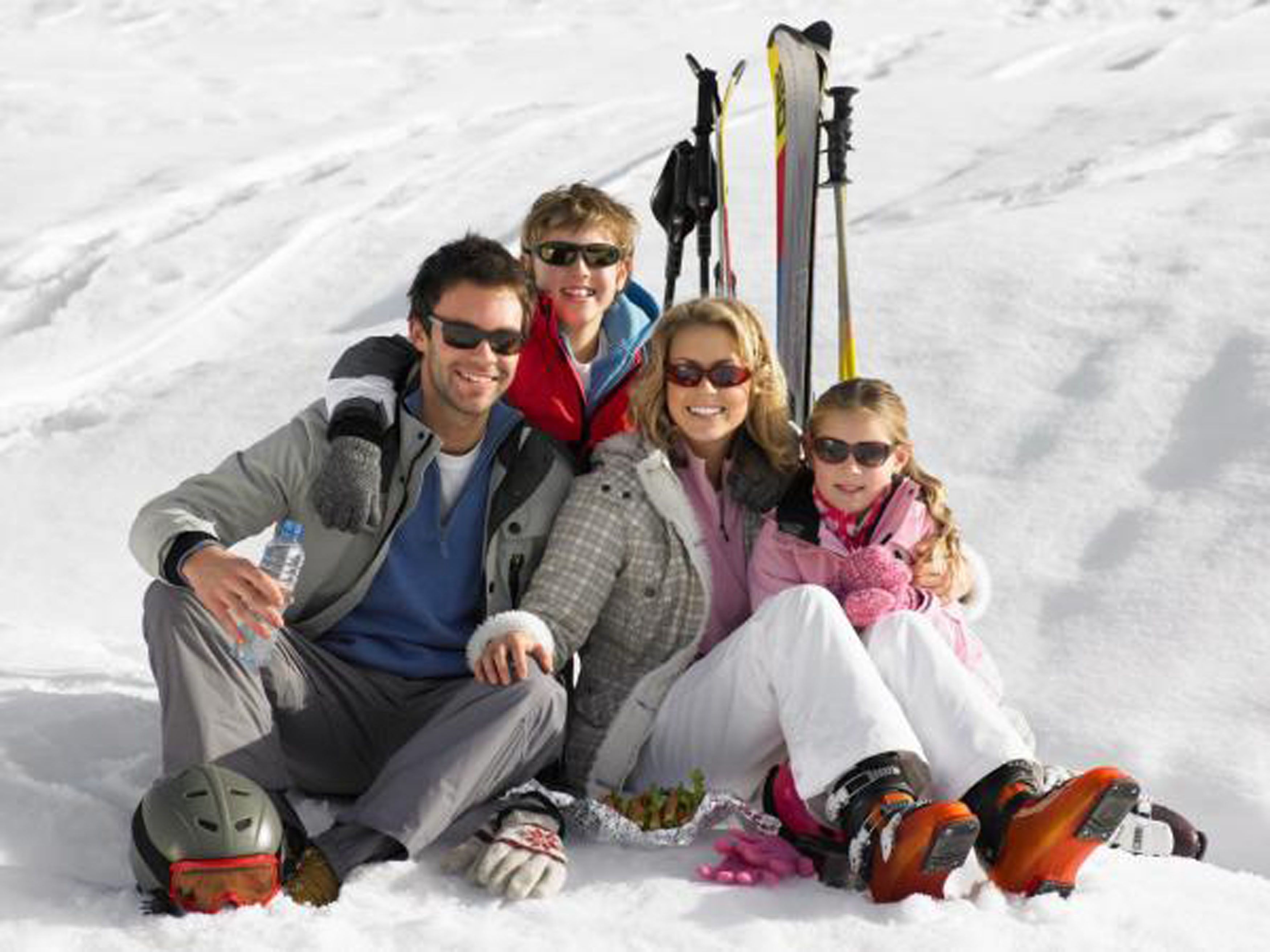 A group of people sitting on the snow with skis and ski poles beside them.