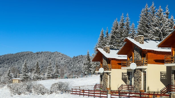 A chalet-style building with a stone facade, wooden balconies, and a snow-covered roof. - Villa Mtashi (Borjomi)