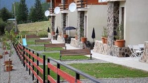 A hotel with outdoor seating, stone pillars, and a red and black fence. - Villa Mtashi (Borjomi)