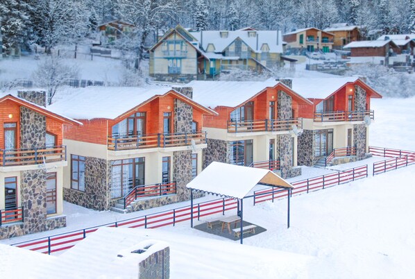 A row of modern cabins with stone facades and red roofs, surrounded by snow-covered trees. - Villa Mtashi (Borjomi)