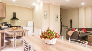 A modern kitchen with white appliances, a dining table with chairs, and a living area with a sofa and cushions. - Villa Mtashi (Borjomi)