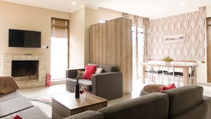 A modern living room with a fireplace, grey sofas, a dining area with a table and chairs, and a TV mounted on the wall. - Villa Mtashi (Borjomi)