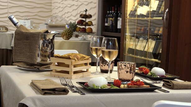 Una mesa servida para una comida, con copas de vino, una botella de vino y una exposición de frutas.