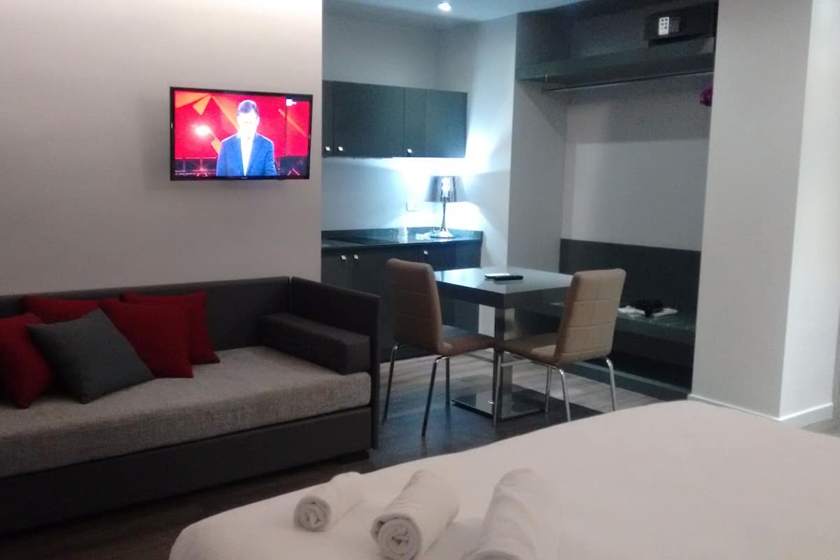 A hotel room with a sofa, a TV mounted on the wall, a desk, and a chair.