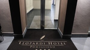 Entrada de un hotel con un felpudo negro que dice "LEOPARDI HOTEL POMIGLIANO" y un logotipo con una pluma.
