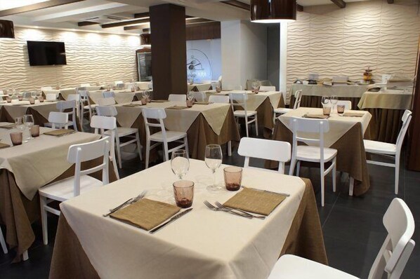 Un restaurant avec de nombreuses tables dressées pour le service, chacune étant agrémentée de chaises et de nappes blanches.