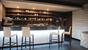 Zona de bar moderna con una barra larga, taburetes blancos y estantes llenos de botellas.