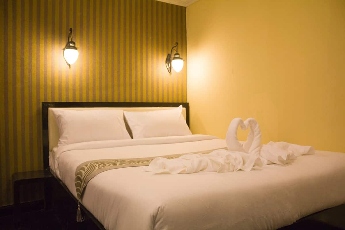 Une chambre d’hôtel avec un lit, deux lampes fixées au mur et une serviette décorative posée sur le lit.