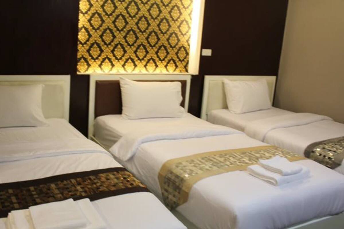 Une chambre d’hôtel avec trois lits simples, chacun doté de draps et d’oreillers blancs. Un rideau à motifs est accroché au-dessus des lits, et il y a une fenêtre avec des stores.