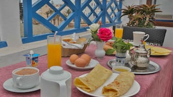 Una mesa de desayuno con una taza, un vaso de jugo de naranja, huevos, pan y una tetera.