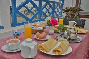 A breakfast table with a cup, a glass of orange juice, eggs, bread, and a teapot.