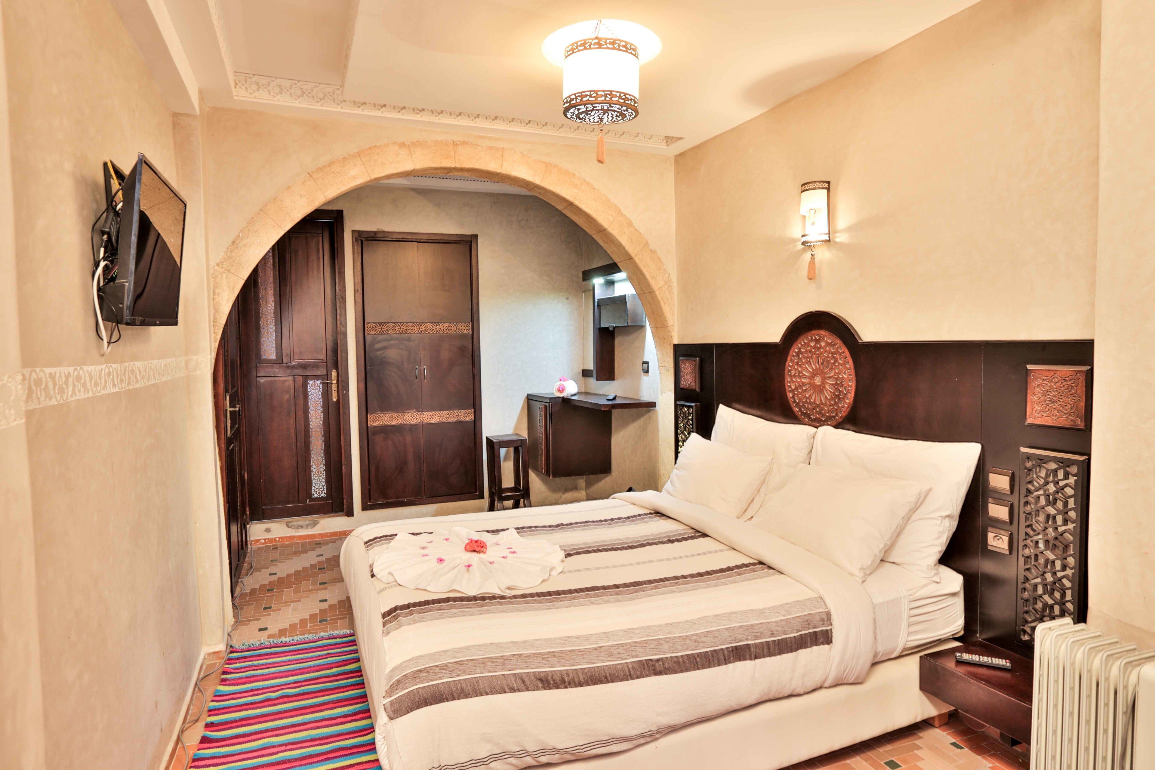 A hotel room with a large bed, a TV mounted on the wall, a desk, and a decorative wall piece.