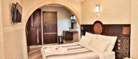 A hotel room with a large bed, a TV mounted on the wall, a desk, and a decorative wall piece.