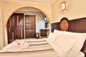 A hotel room with a bed, a desk, and an arched doorway.