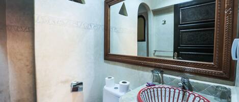 Un baño con inodoro blanco, lavamanos de cuenca roja y espejo con marco de madera.