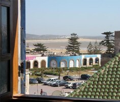 Vista de una zona costera con un estacionamiento, un edificio de paredes azules y blancas, y una playa al fondo.