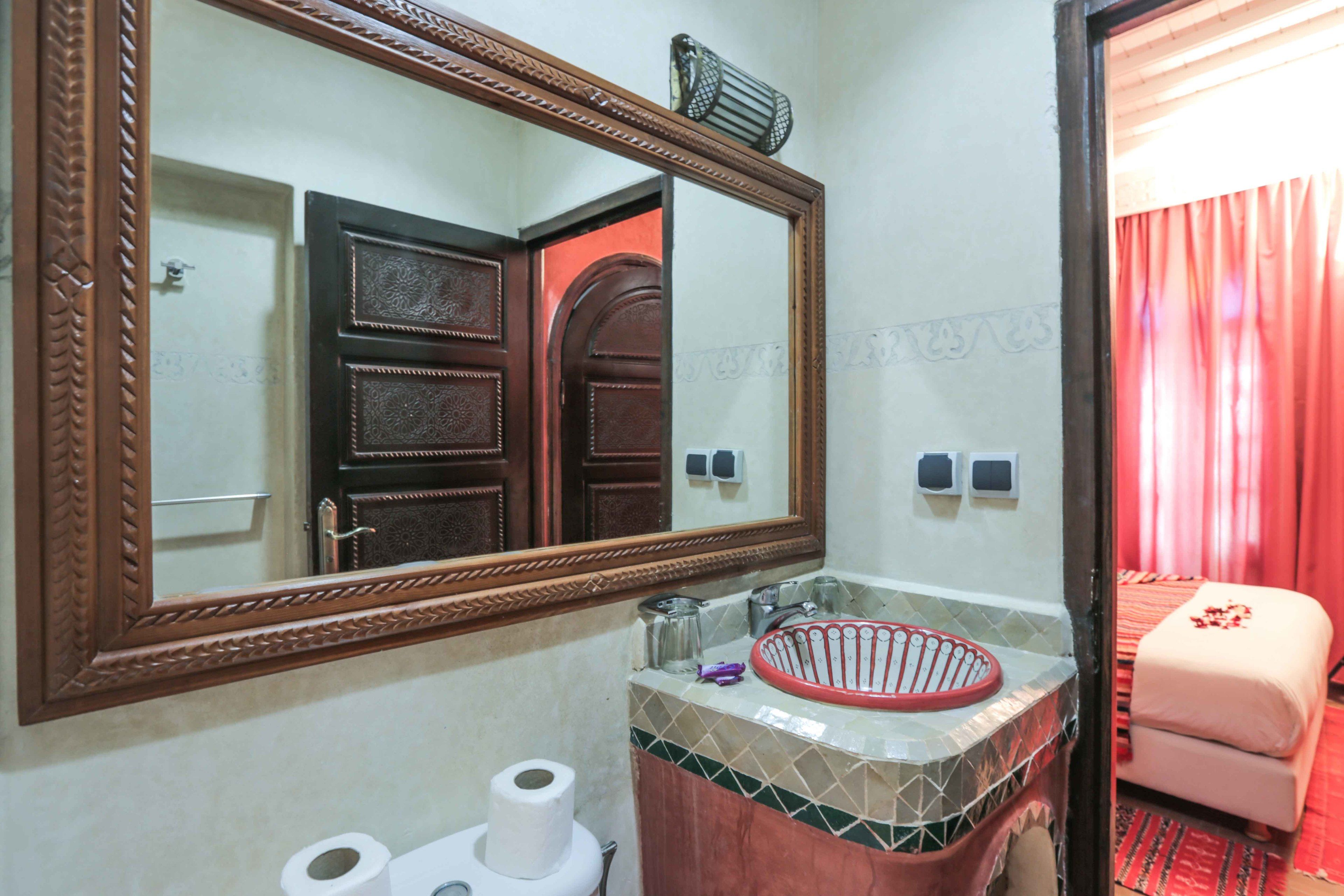 A bathroom with a large mirror, a sink with a red basin, and a toilet.