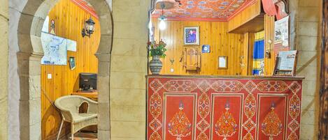 A reception area with a wooden desk, a wicker chair, and a decorative red panel with floral patterns.