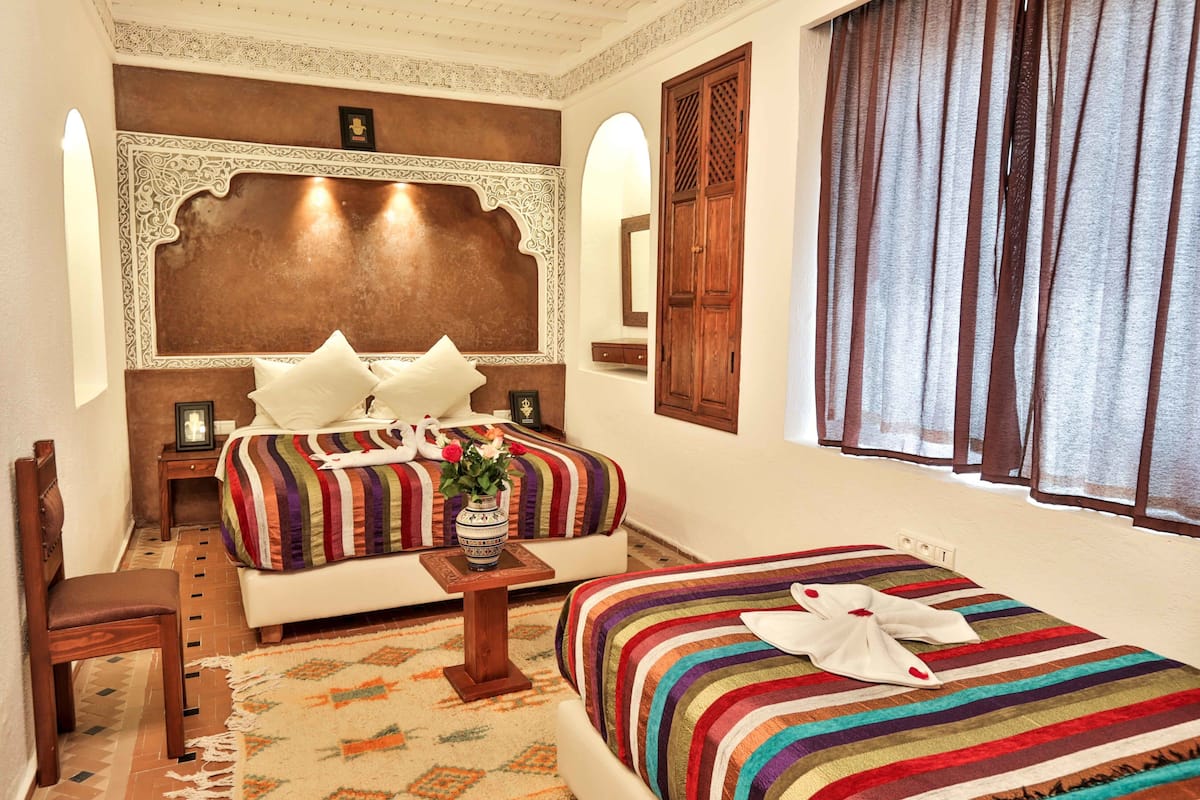 A hotel room with two beds, a sitting area, and a decorative headboard.
