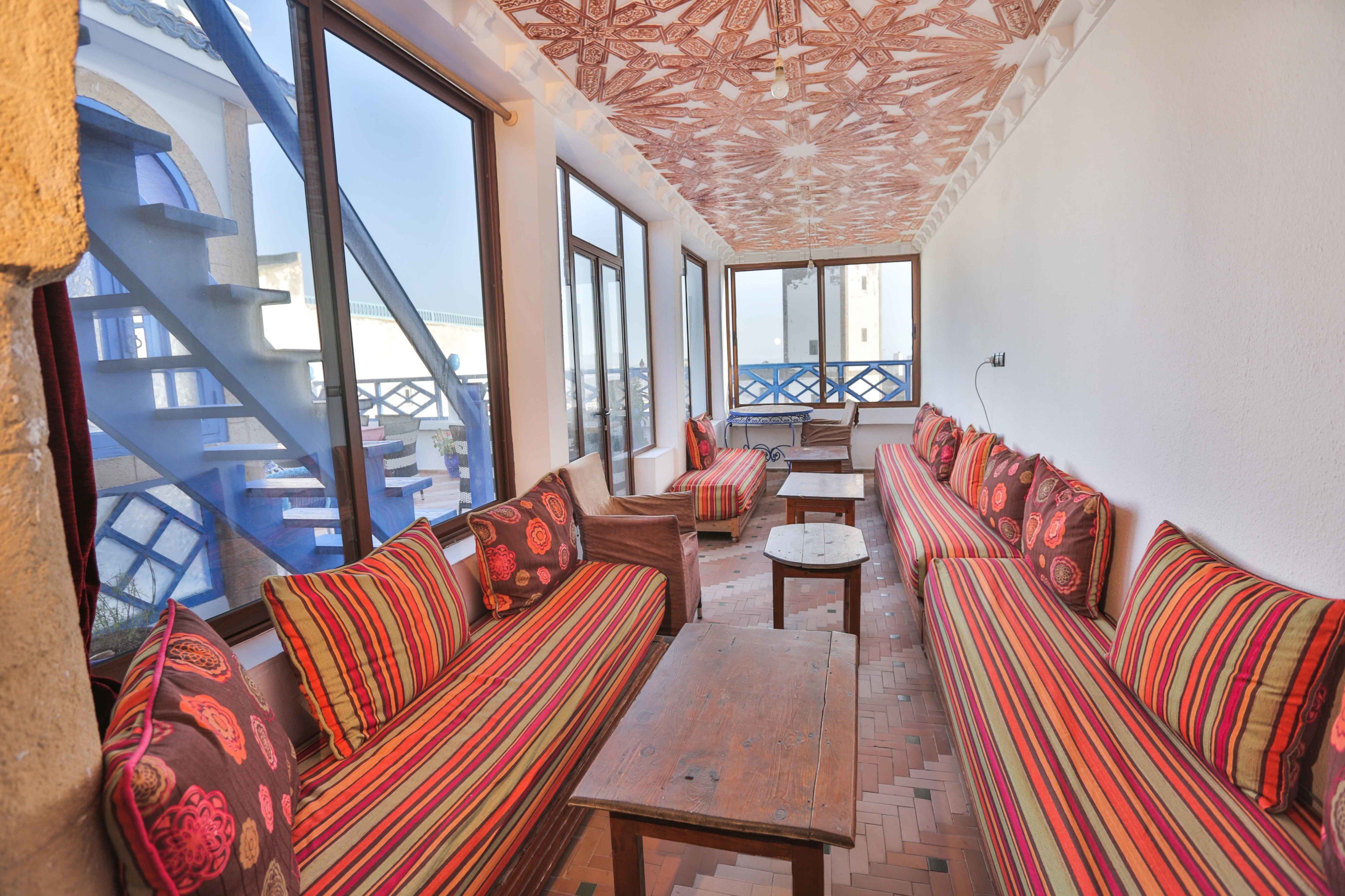 Un balcone luminoso con divani a righe, un tavolo di legno, ampie finestre e un soffitto decorato.