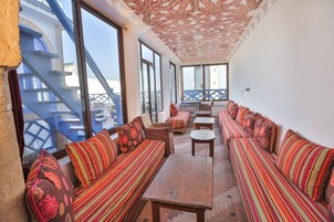 Un balcone luminoso con divani a righe, un tavolo di legno, ampie finestre e un soffitto decorato.