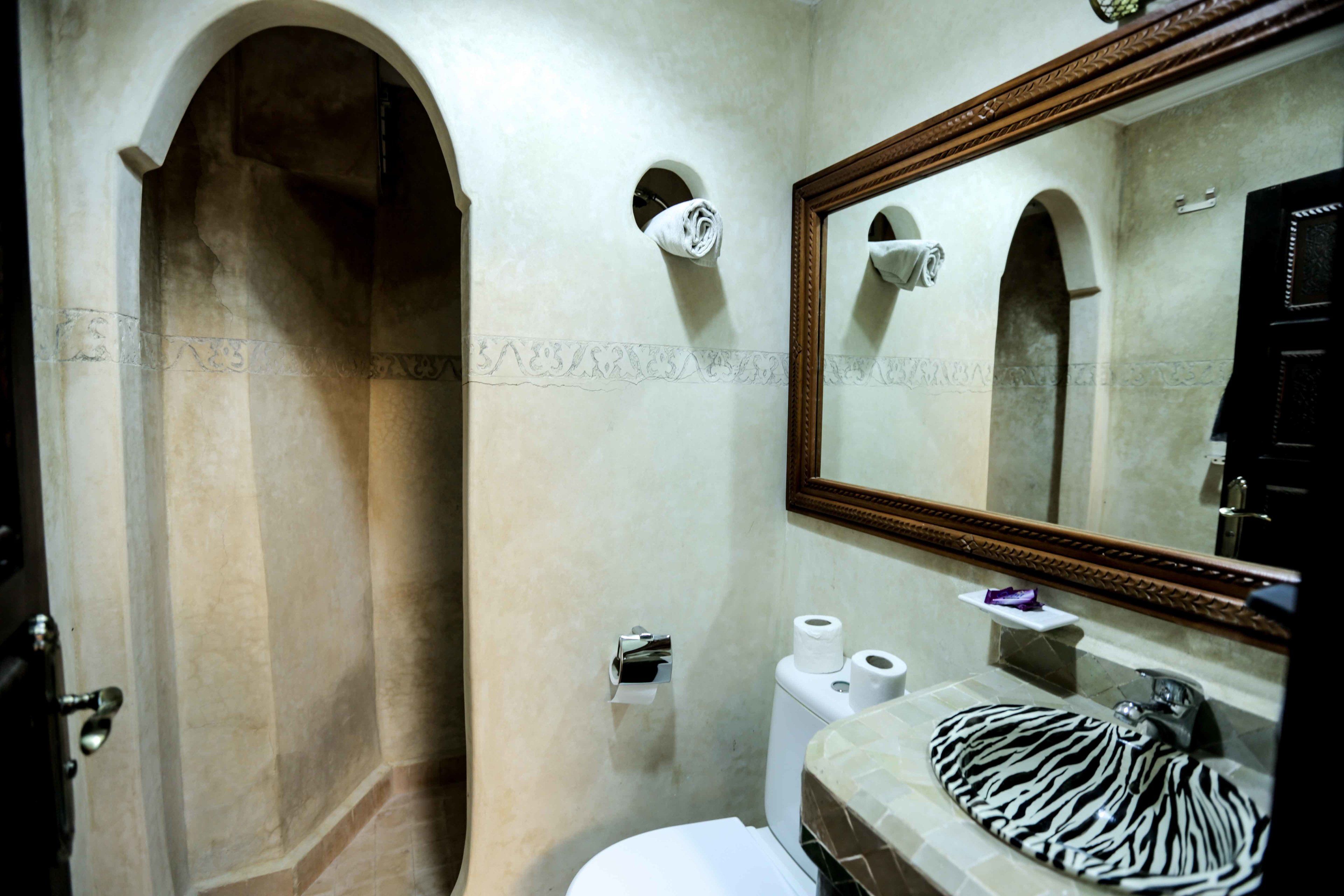 Ein Badezimmer mit Marmorwand, einem spiegel mit Holzrahmen, einem Waschbecken mit Zebra-Muster und einer Toilette mit zwei Toilettenpapierrollen.