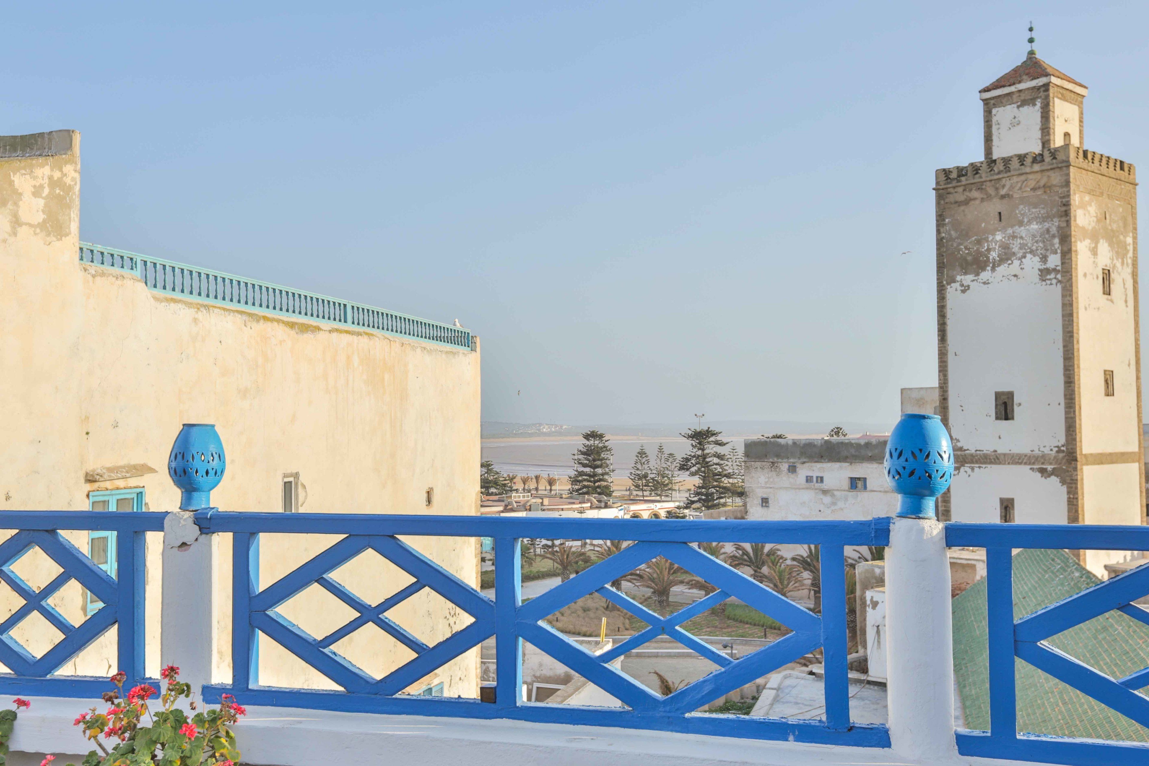A balcony with blue railings overlooking a coastal area with buildings and a tower.