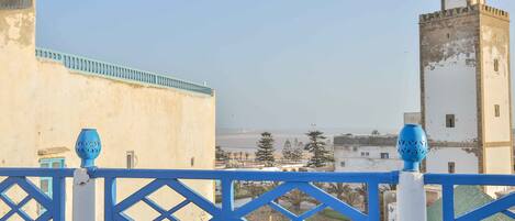 A balcony with blue railings overlooking a coastal area with buildings and a tower.