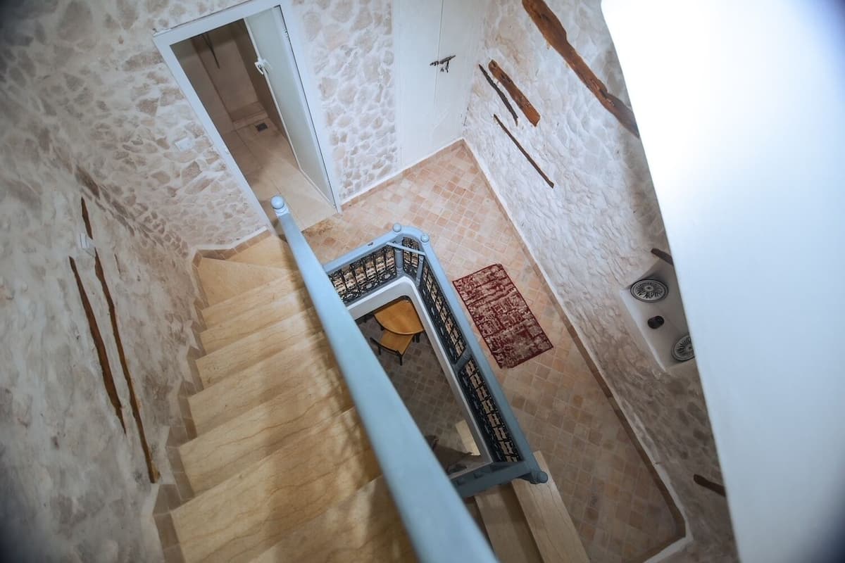 A spiral staircase with a wooden finish, leading to a room with a tiled floor and a red rug.