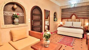 A hotel room with a bed, sofa, and a table with a vase of flowers. - Riad Nakhla (Essaouira)