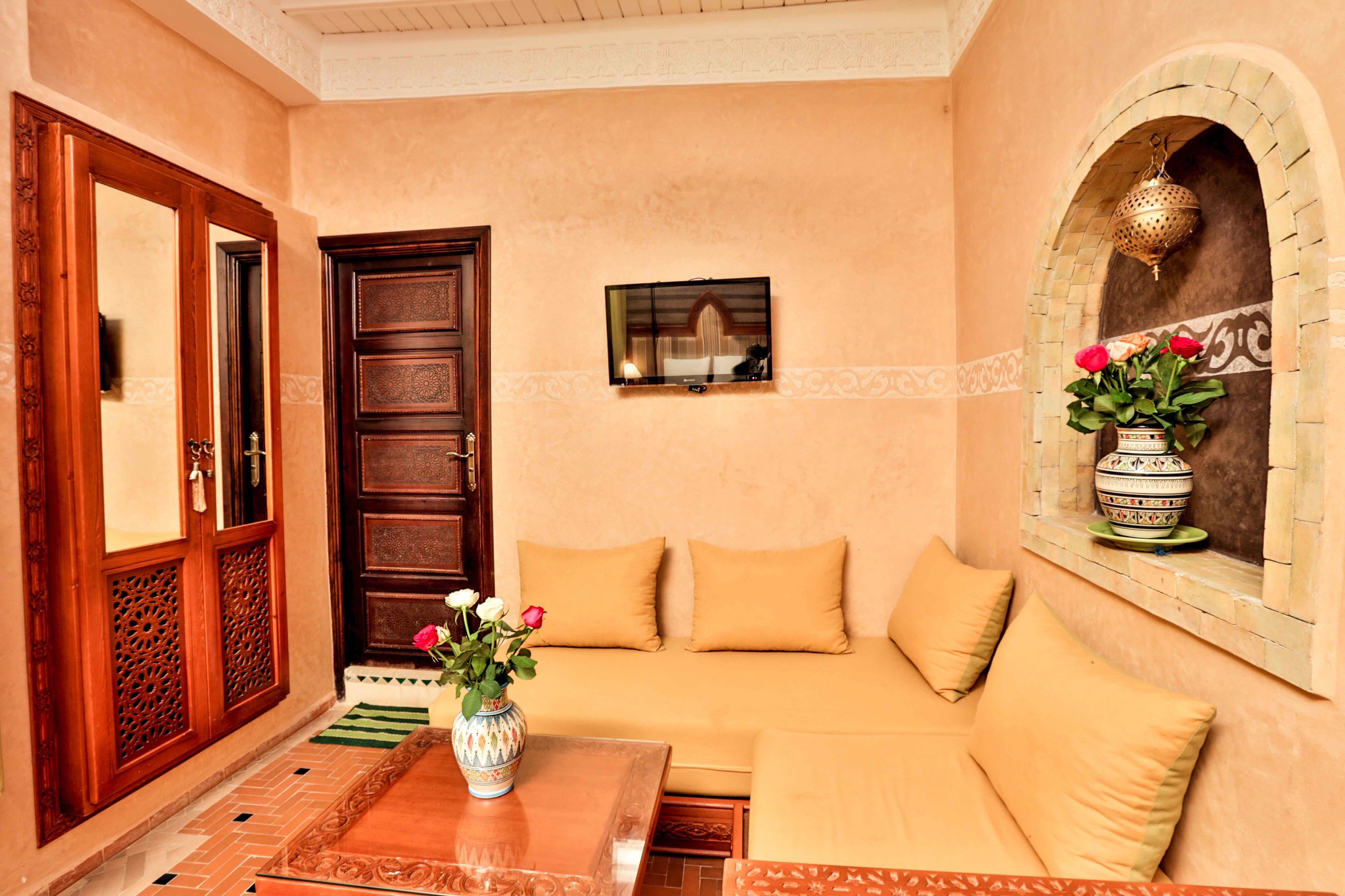 A room with a beige sofa, a wooden door, a small table with a vase of flowers, and a decorative wall piece.
